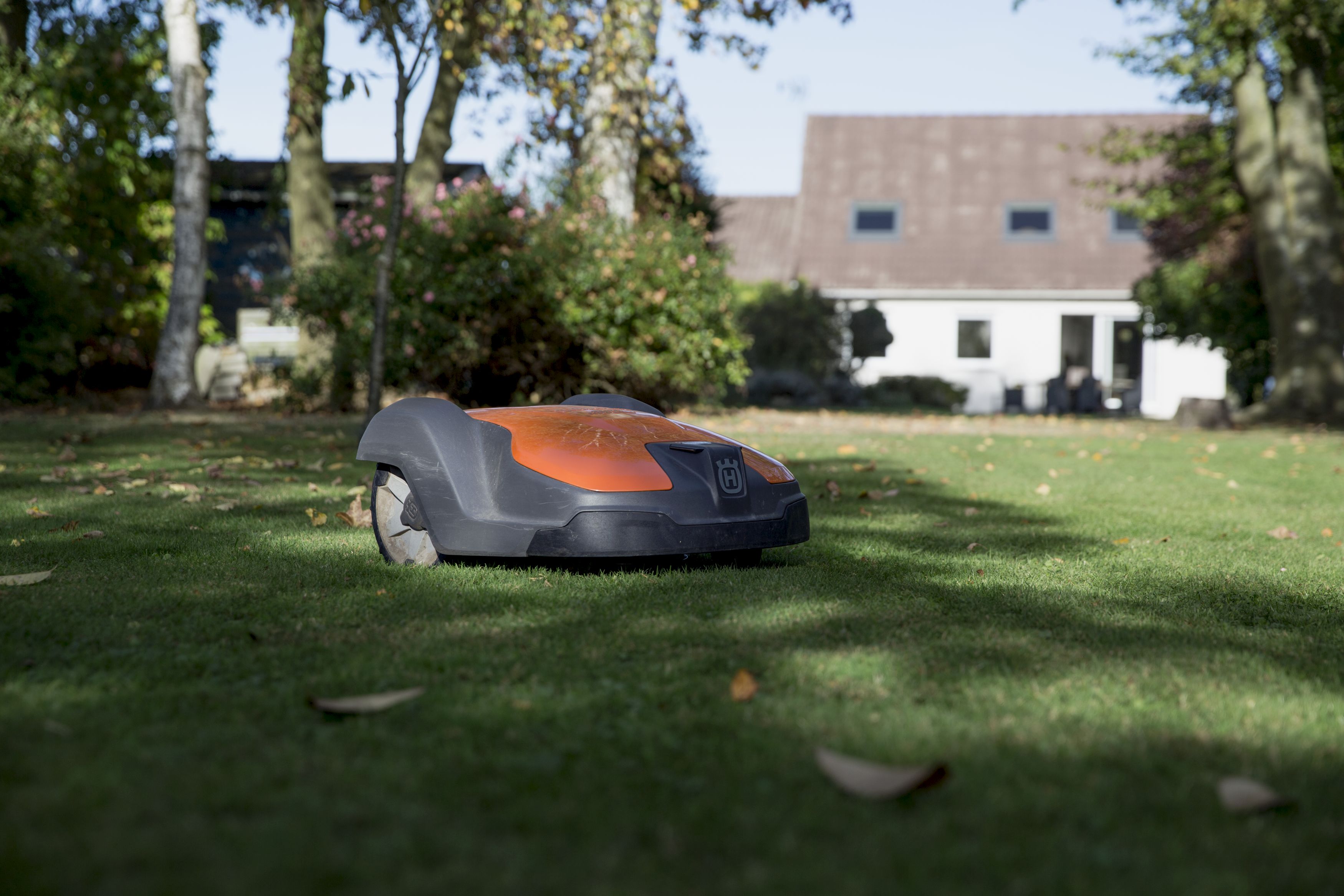 melns ar oranžu zāles pļāvēja robots no sāna skata pļaujot zāli